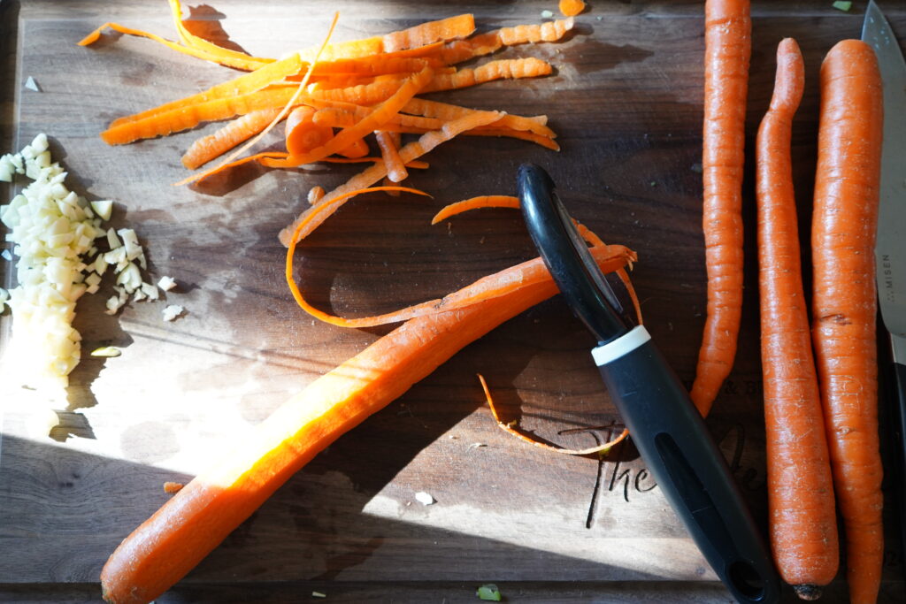 a cutting board with carrot being peeling with a potato peeler