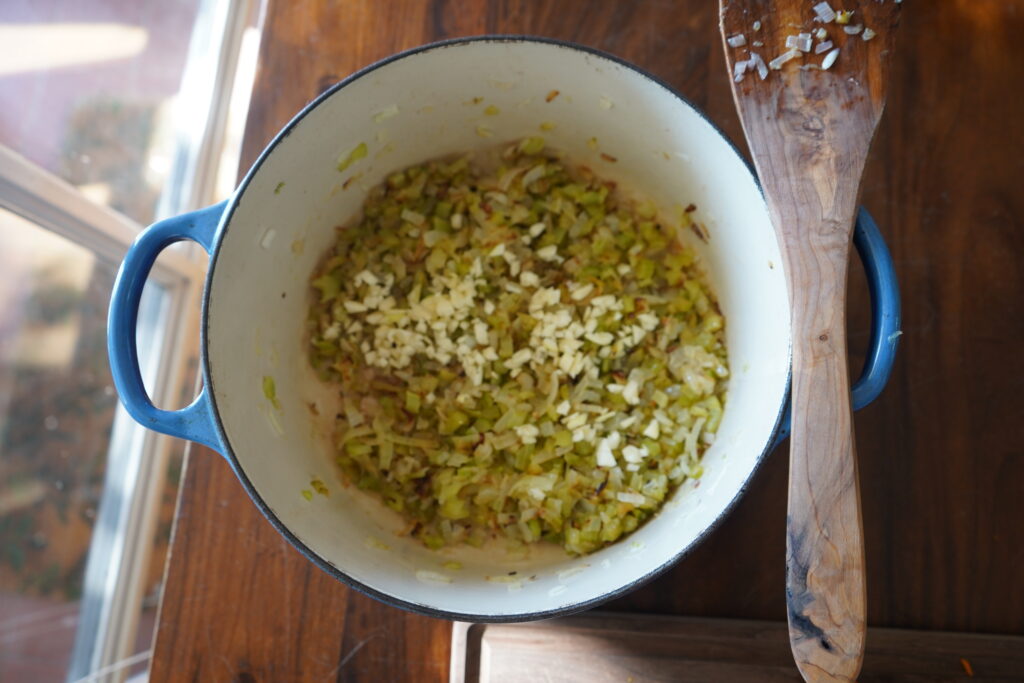 a Dutch oven with sauteed vegetables at the bottom and fresh garlic added