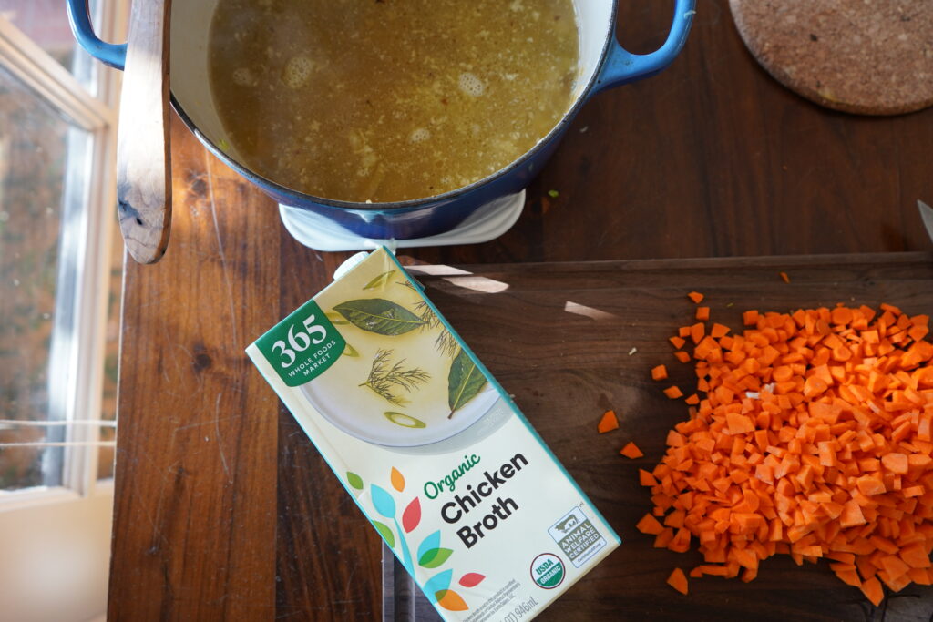 a box of organic chicken broth on a cutting board next to a pile of chopped carrots