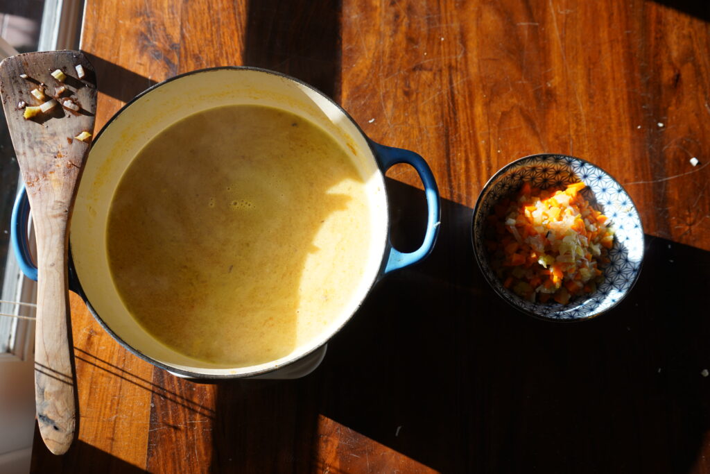 a pot of soup next to a bowl of cooked vegetables