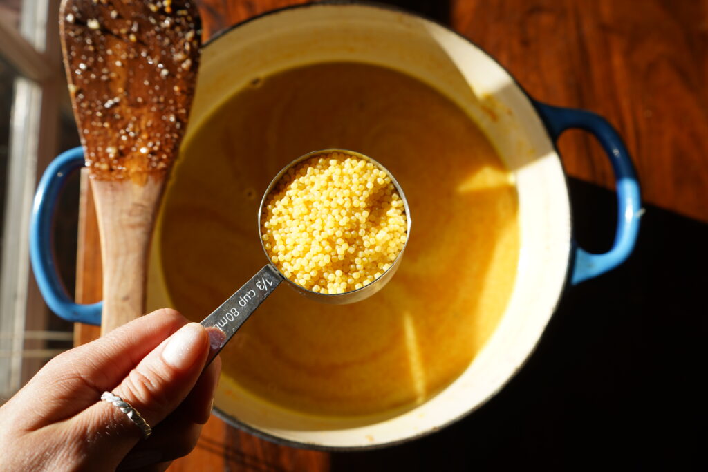 tiny pasta in a measuring cup over a pot of soup