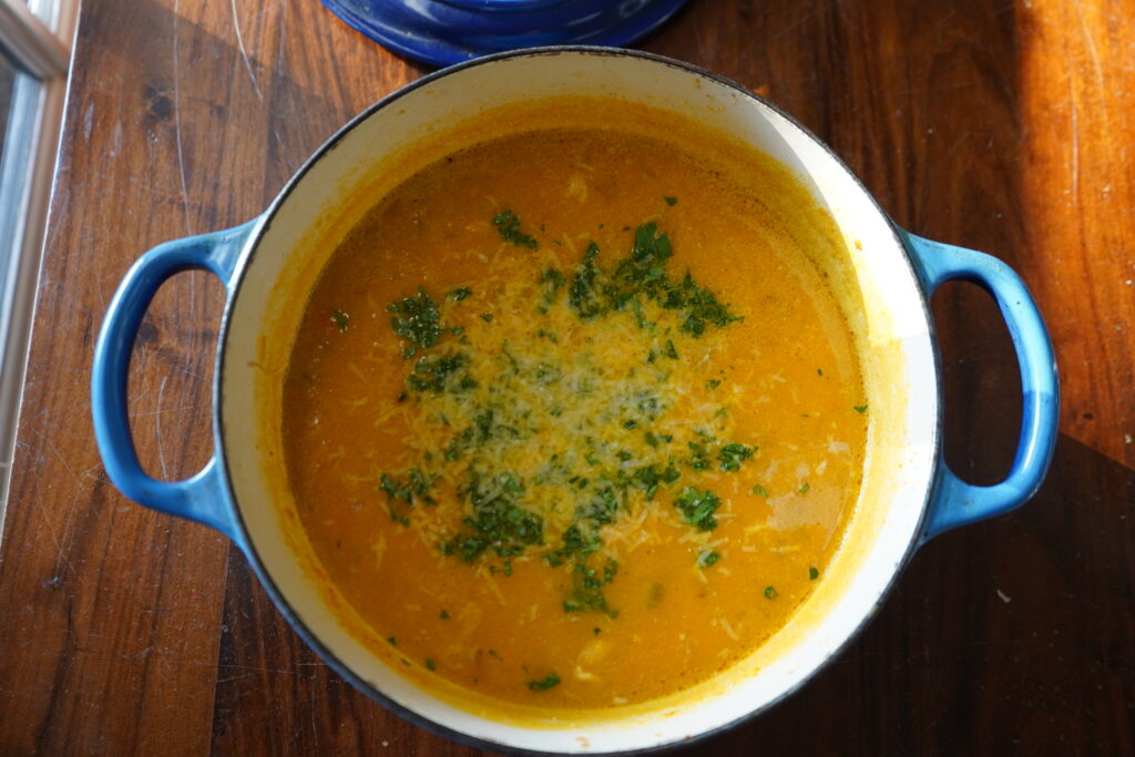 a Dutch oven of yellow soup with parmesan sprinkled on top