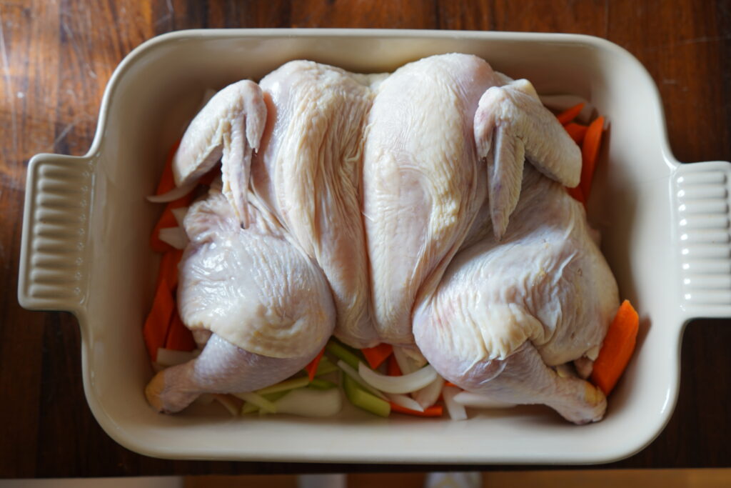 Whole chicken, butterflied open over chopped vegetables.