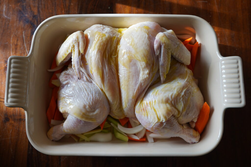 Whole chicken butterflied in a pan drizzled with olive oil .