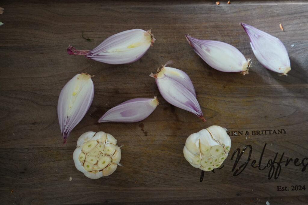 Garlic and shallots that have been chopped longways for the shallots and the tops of the garlic are chopped off.