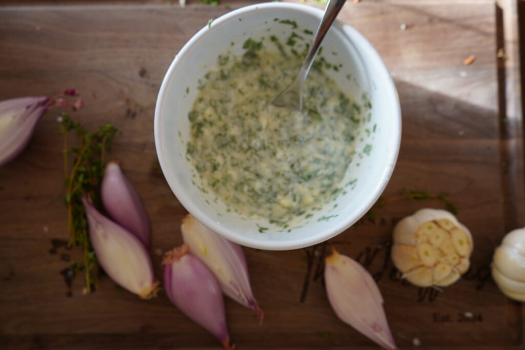 Garlic herb butter in a bowl, surrounded by shallots and garlic.