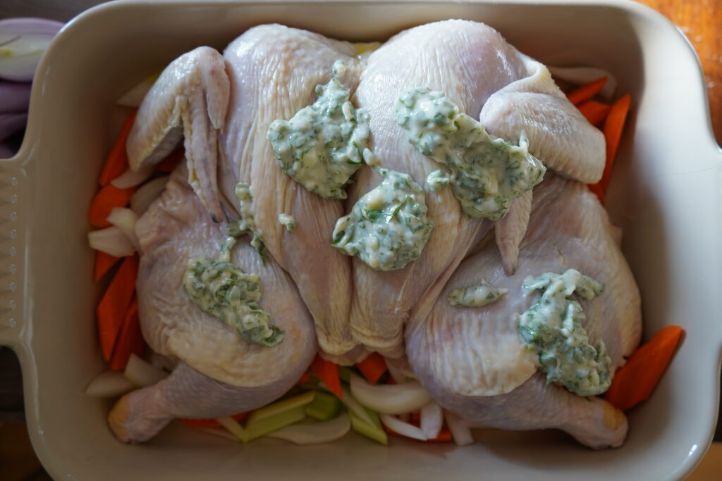 Whole chicken in a baking dish covered in garlic herb butter.