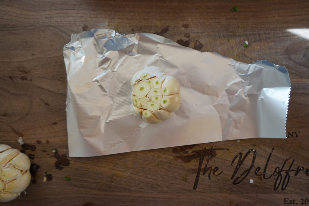 A whole garlic that is sitting on foil ready to be wrapped in it.