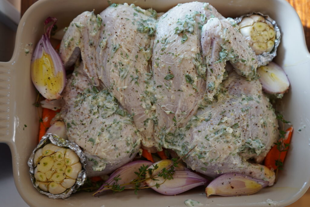 A whole chicken in a pan, covered in garlic herb butter, ready to be baked.