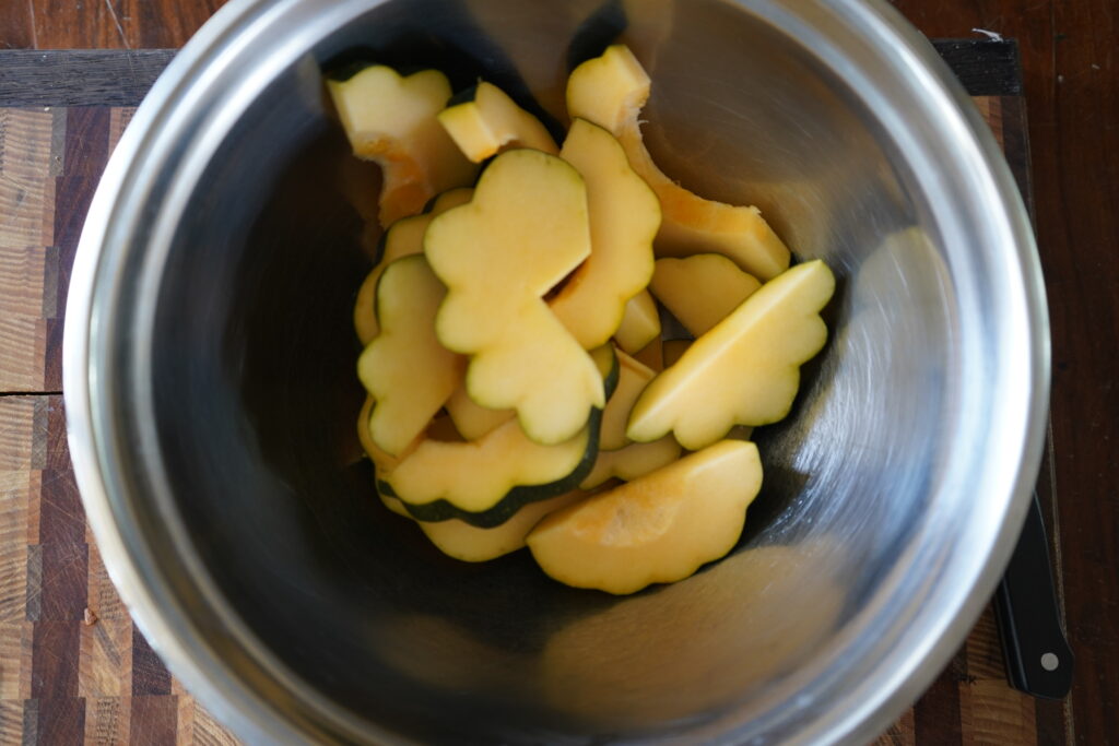 Cut up acorn squash in a metallic bowl.