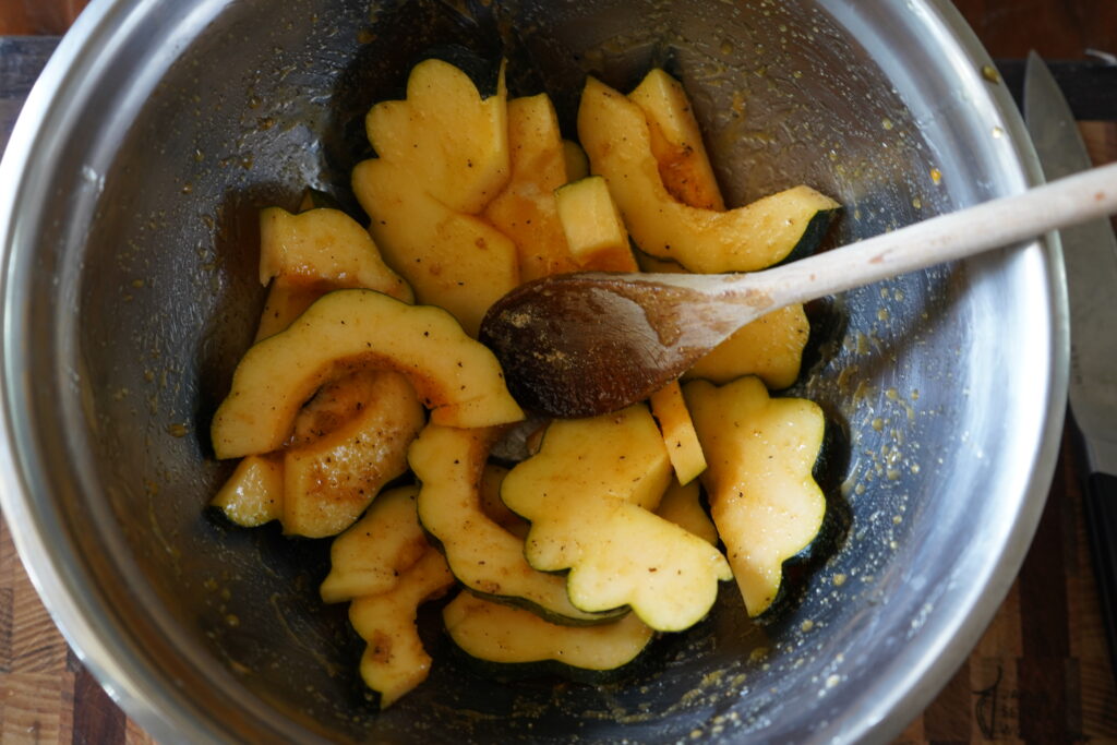 Seasoned cut up acorn squash in a mixing bowl.