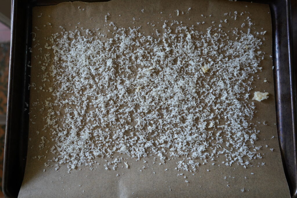 A baking sheet covered in parchment paper, on the parchment paper is sprinkles of parmesan cheese.