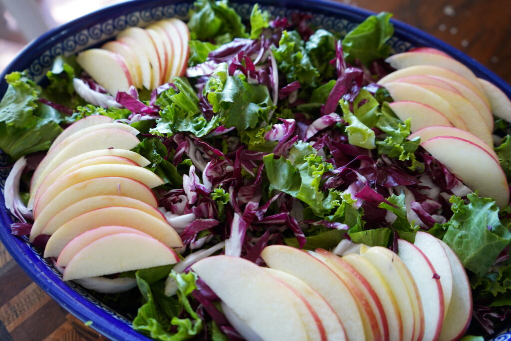 A bowl of salad with apples and greens inside.