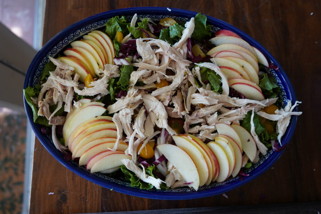 A huge blue salad bowl full of vegetables and fruit and chicken.