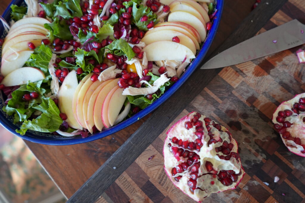 A cut up pomegranate on a cutting board next to a big salad.