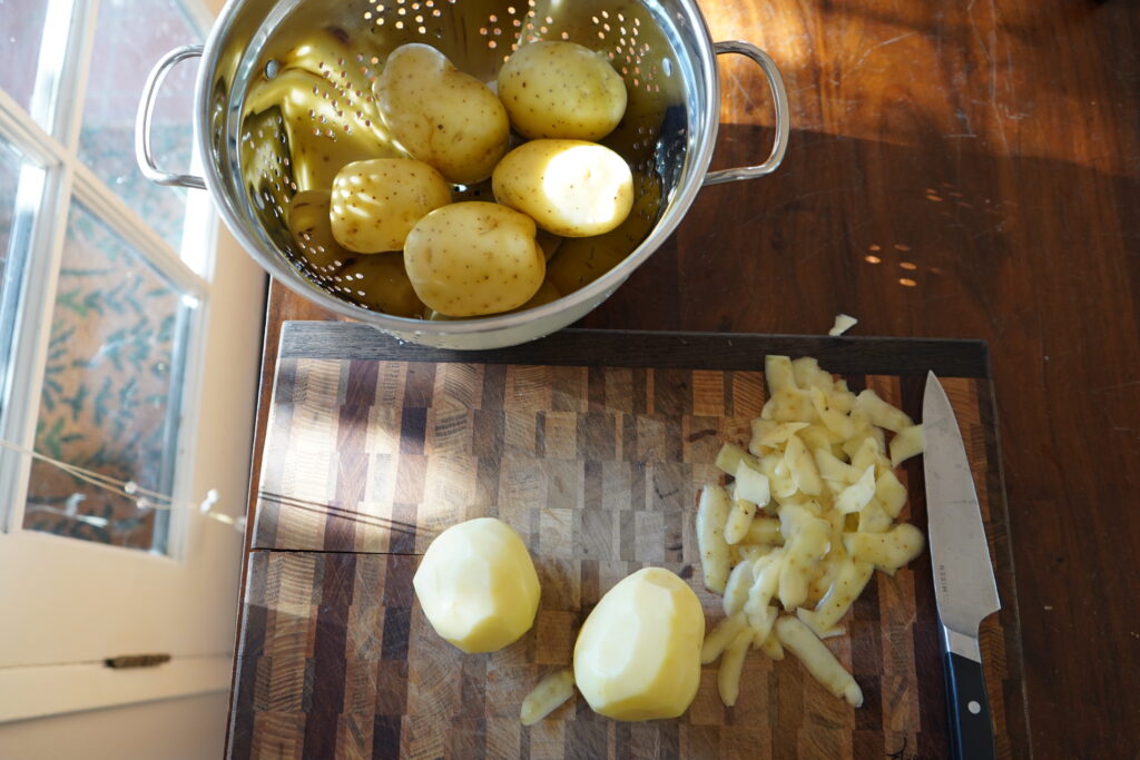 5 golden potatoes in a strainer and 2 golden potatoes being peeled