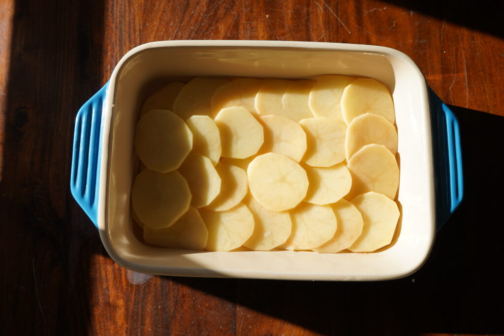 A baking dish with thinly sliced potatoes laying inside