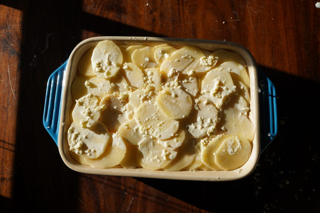 Thinly sliced potatoes in a baking dish covered in heavy cream