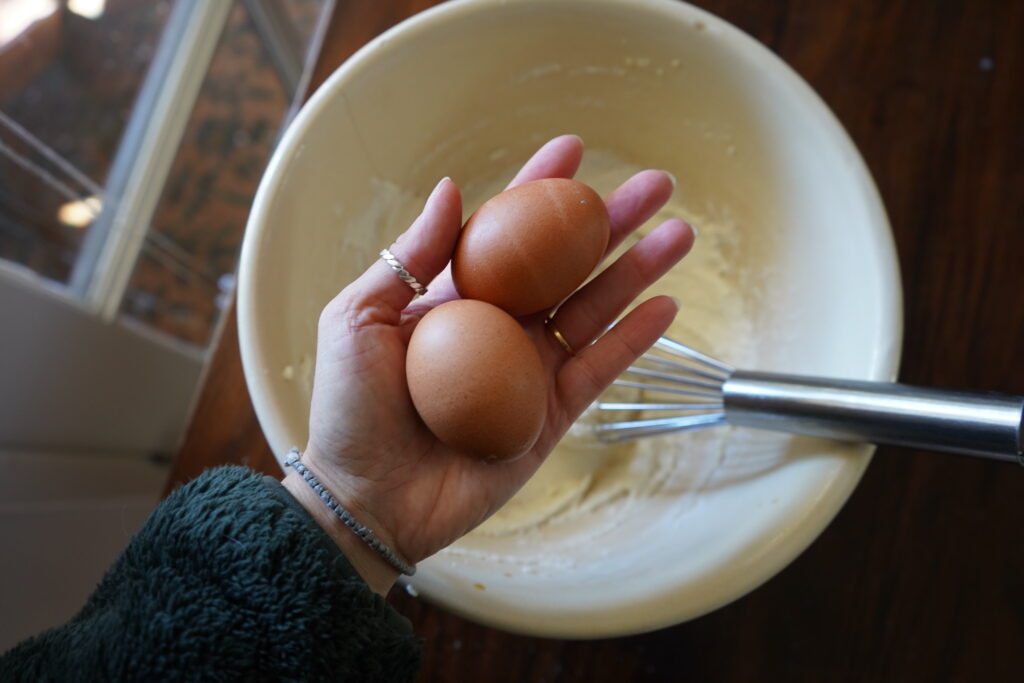 A hand holding two brown eggs over a bowl