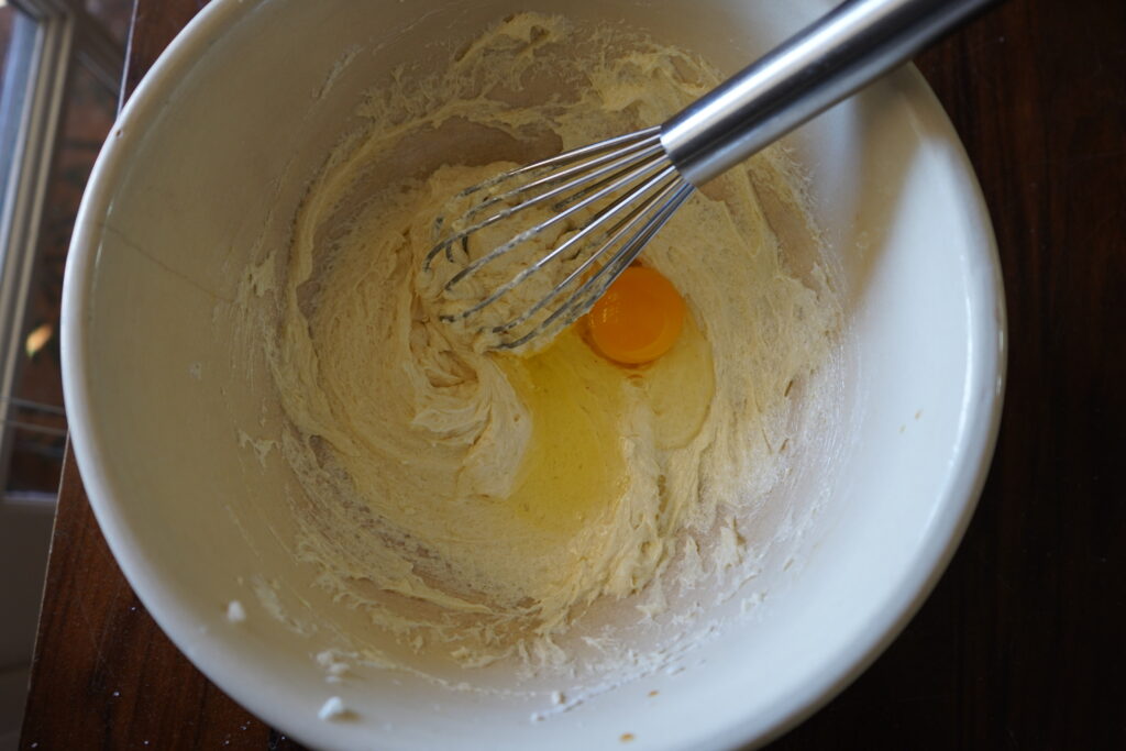 A mixing bowl with a sugar and butter paste on the bottom with an egg ready to be mixed in