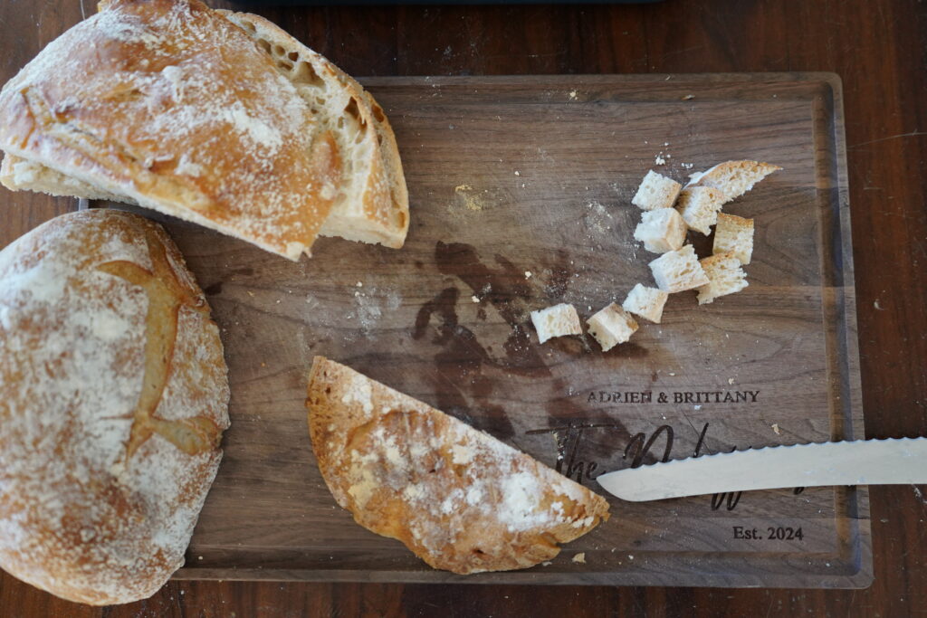 a loaf of sourdough bread being cut up into cubes on a wooden cutting boards