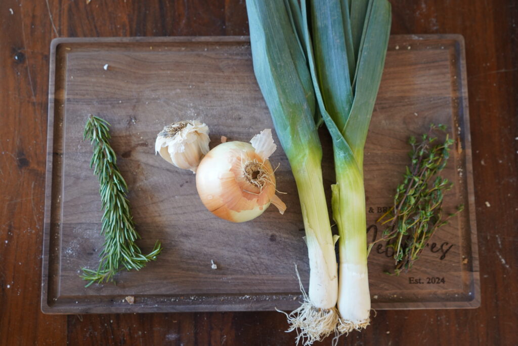 rosemary, garlic, onion, leeks and thyme on a cutting board