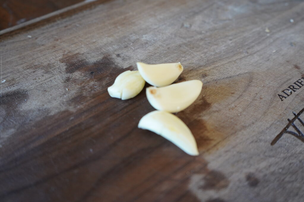 4 cloves of whole garlic on a wooden cutting board