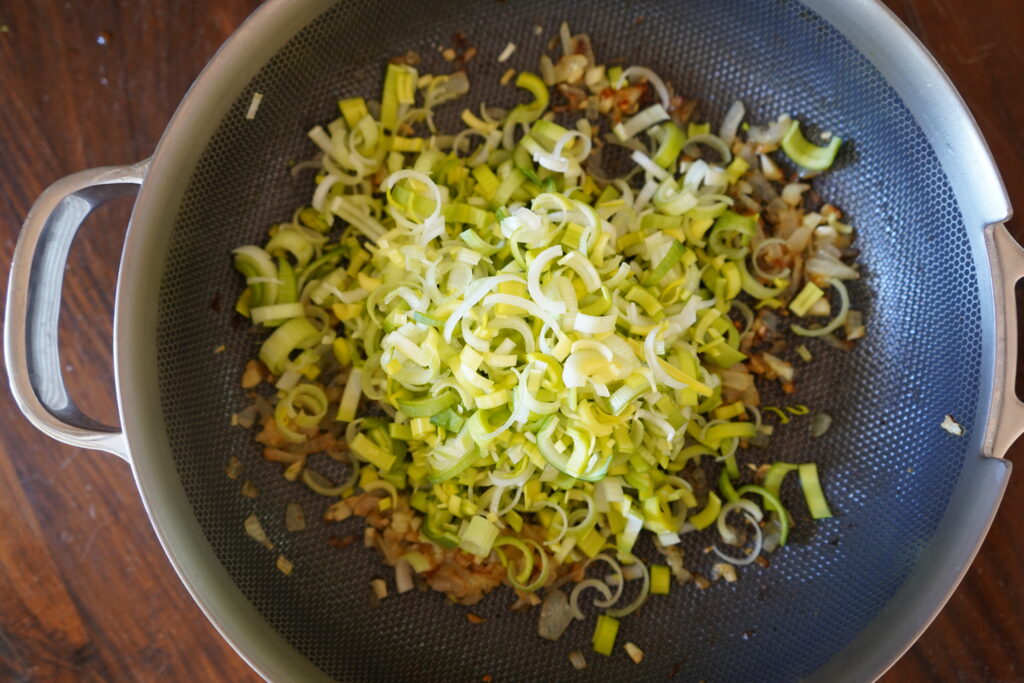 freshly chopped leeks being added to a pan of browned onions