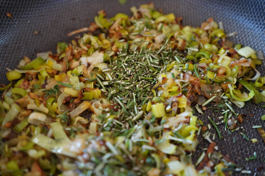 chopped rosemary added to a pan of leeks and onions