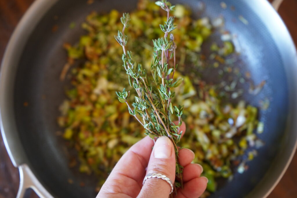 fresh sprigs of thyme being held over a pan of cooked vegetables