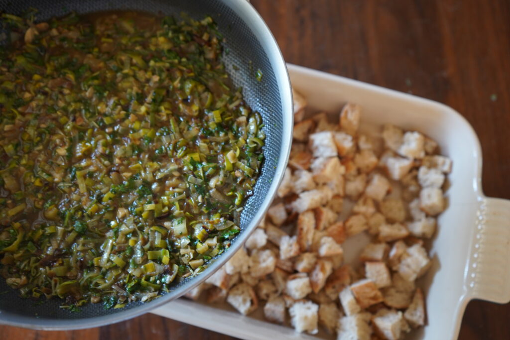 a hot pan of vegetables hovering over a pan of hot bread cubes