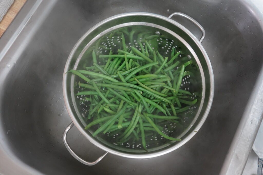 boiled green beans in a strainer in the sink