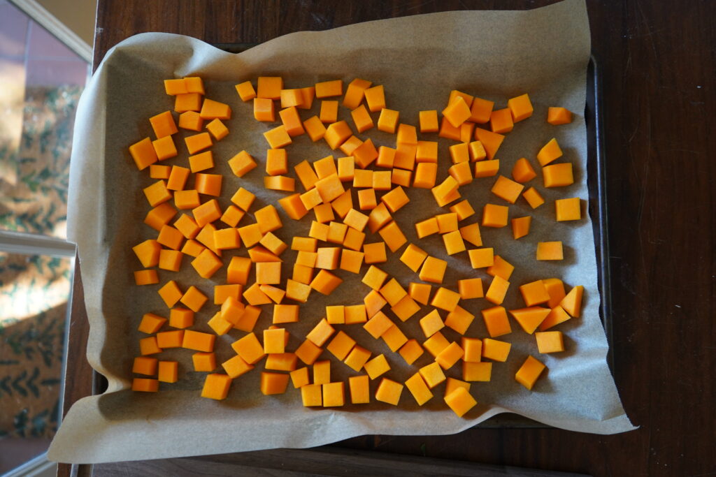 a backing tray that has parchment paper on in and a bunch of cubed butternut squash