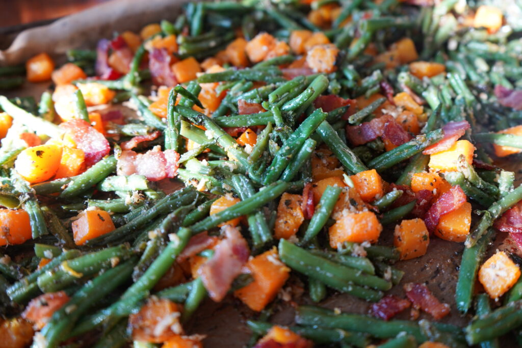 a baking tray with green beans, butternut squash and bacon bits