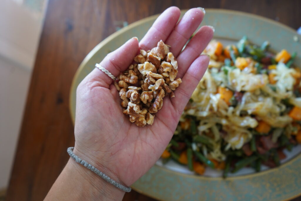 a hand holding baked walnuts over a tray of food