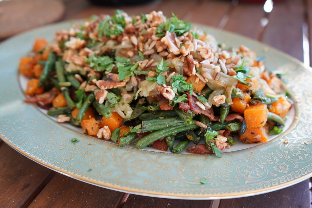  plate of a green bean recipe, full of butternut squash, nuts, bacon and onions