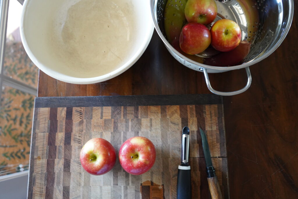 apples on a cutting board next to a potato peeler and a knife
