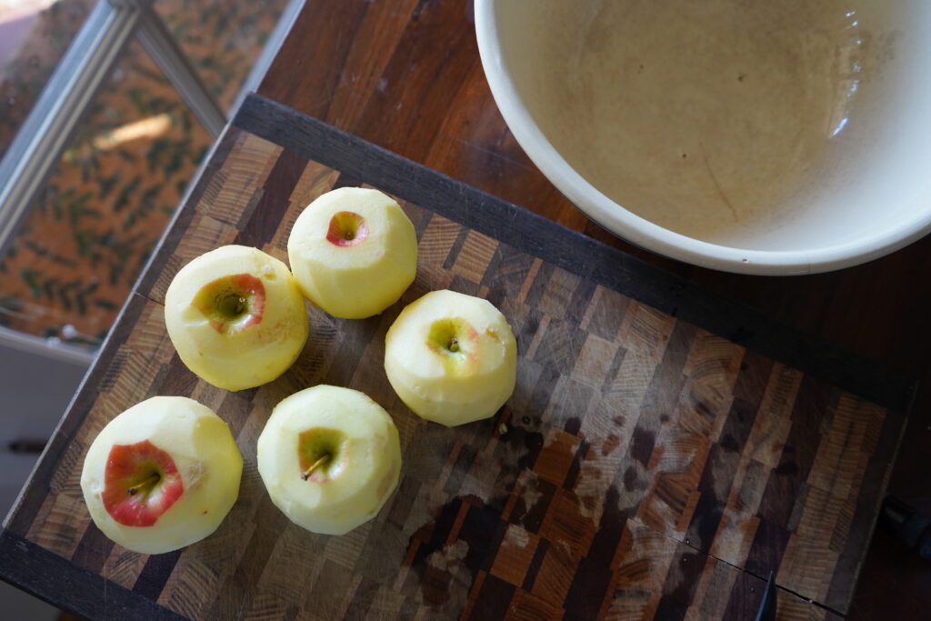 5 peeled apples on a cutting board next to a ceramic bowl