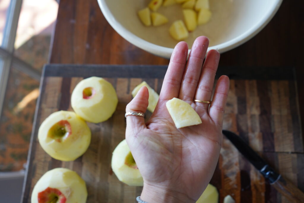 A piece of apple on the palm of a hand being cut for an apple pie