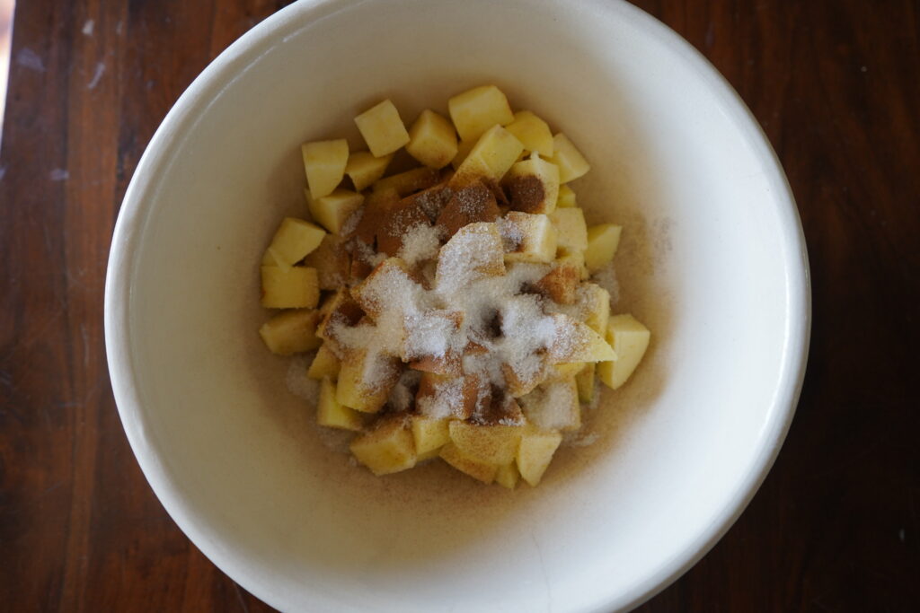 a ceramic bowl full of cut up apples, topped with sugar and cinnamon