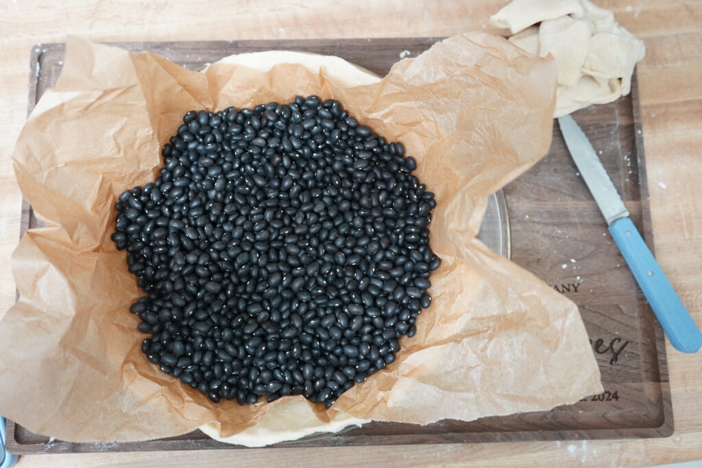 uncooked black beans being used as a weight to pre-cook crust