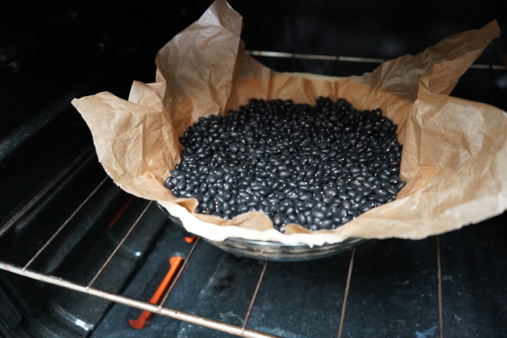 pie crust with uncooked beans, being used as a weight