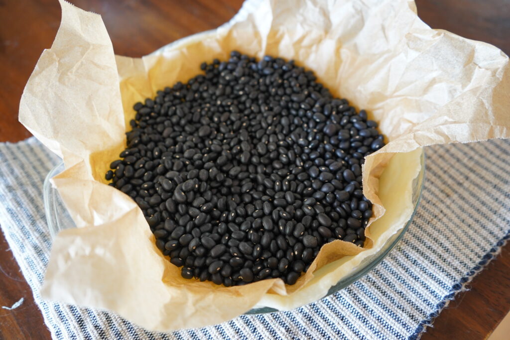 precooked pie crust with the parchment paper and uncooked beans, ready to be removed 