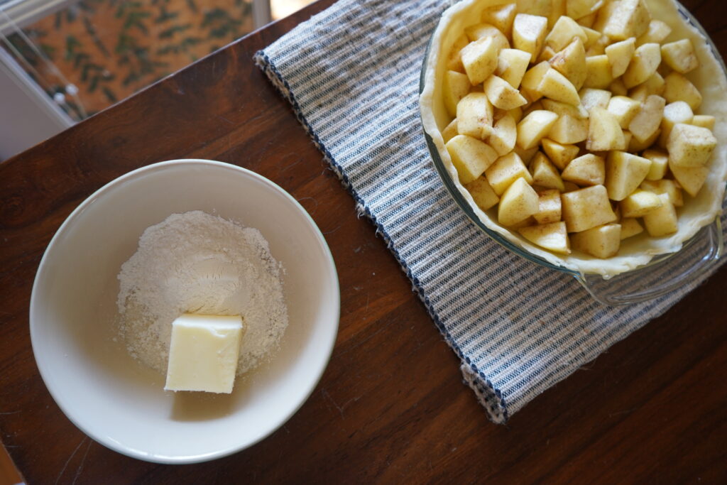 a uncooked pie ready for toppings and a bowl of butter, sugar and flour, ready to be mixed