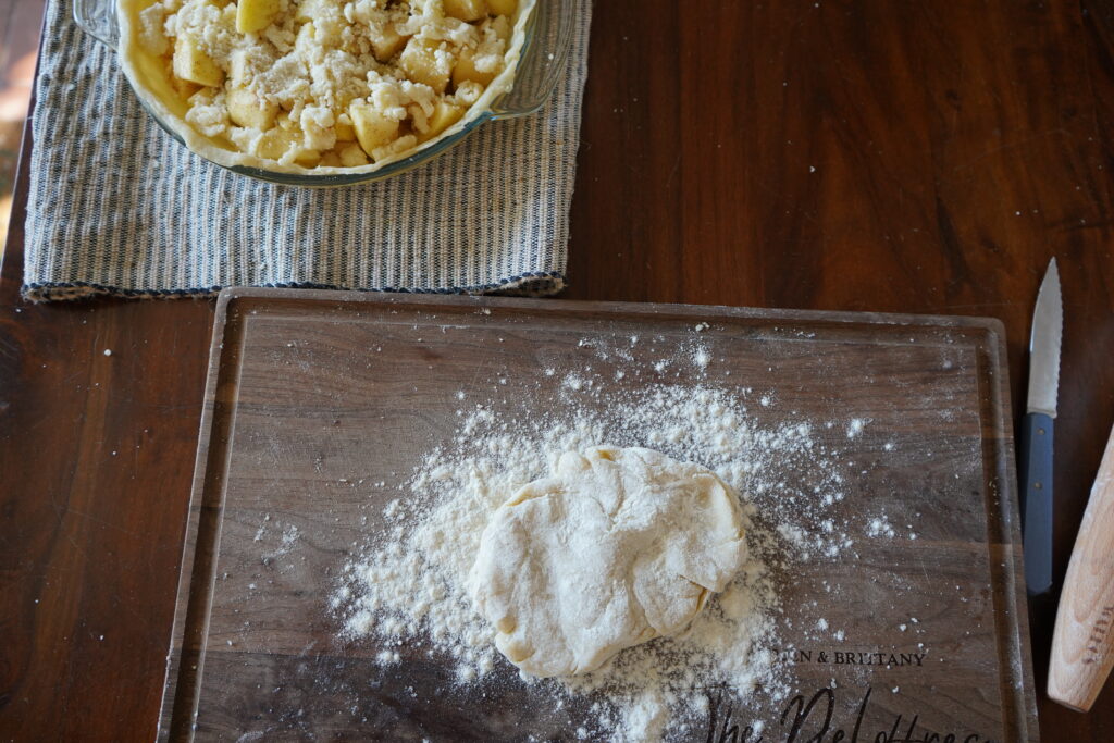 pie crust on a cutting board next to a half built apple pie