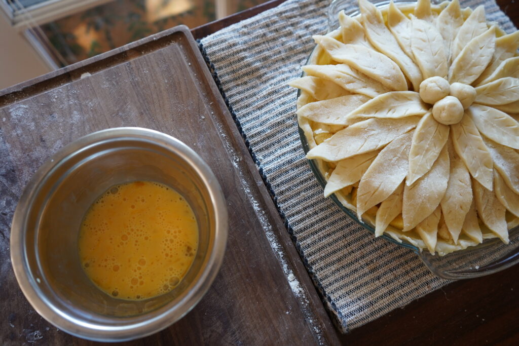 an egg wash bowl next to an uncooked apple pie