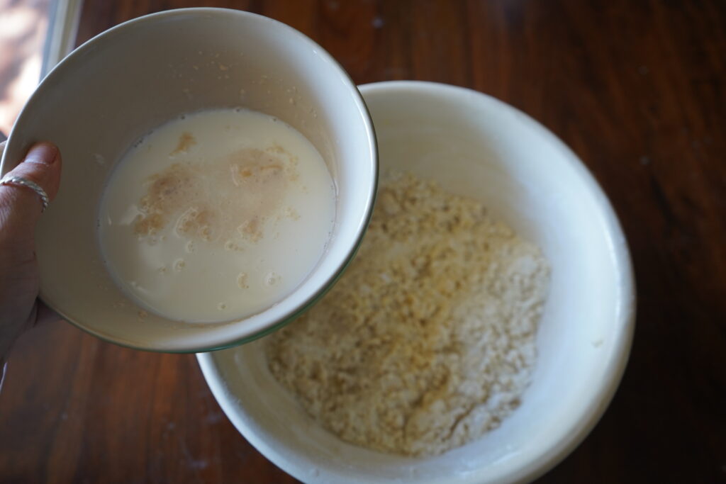 activated yeast mixture being poured into flour in abowl