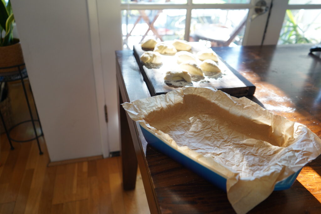 a table with a baking dish on it and floured dough balls on a floured cutting board