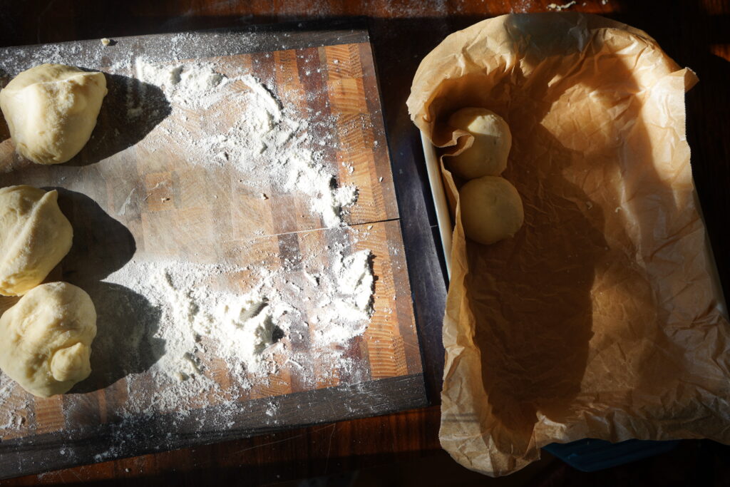 a cutting board with dough on it and to dough balls in a parchment lined baking dish