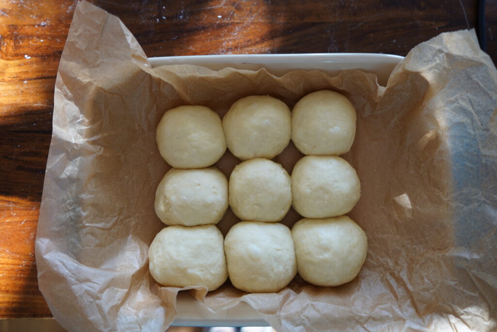 a baking dish lined with parchment paper and filled with nine dinner buns